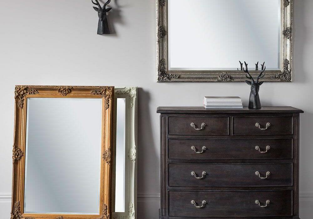Ornate Rectangle Mirror hanging landscape above a chest of drawers with two standing portrait on the floor