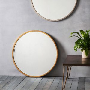 Smith Round Mirror in Gold placed on floor next to table with plant on