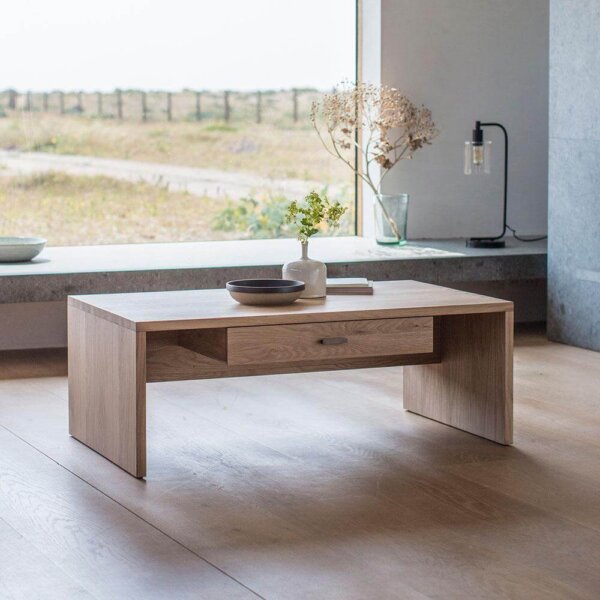 The Serenity Coffee Table positioned in front of a large window with a vase and ornaments on top