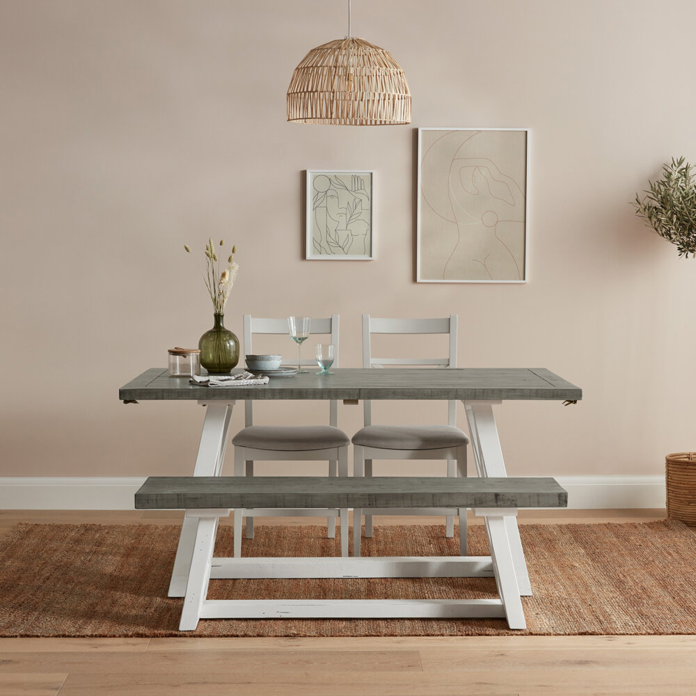 a white and grey extendable dining table with two dining chairs and a dining bench with various items sat atop of the grey tabletop