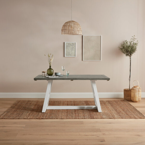 wooden extendable dining table with white base and grey table top sat on wood floor with rug and hung pictures behind