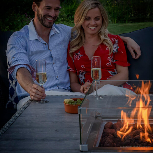 close up of couple sitting with glasses of fizz looking at fire pit dining table