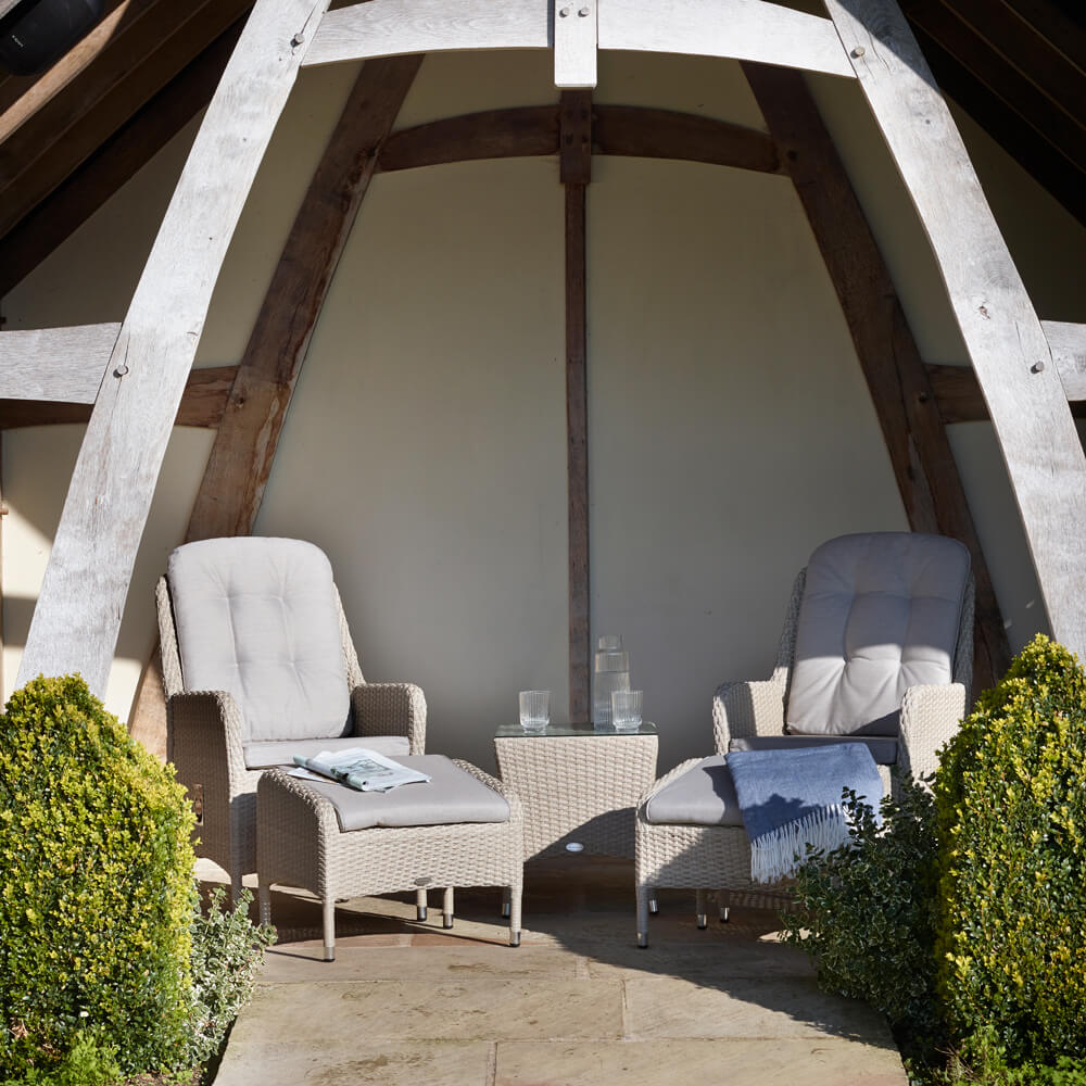 Bramblecrest Tetbury Garden Recliner Chair Set under an awning with a newspaper on one stool and glasses on the side table