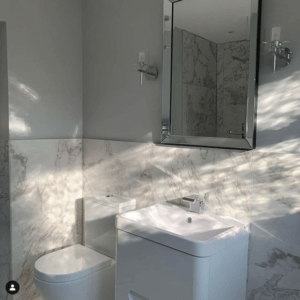 white marble bathroom with white sink and toilet. silver rectangular mirror with 2 wall lights above sink