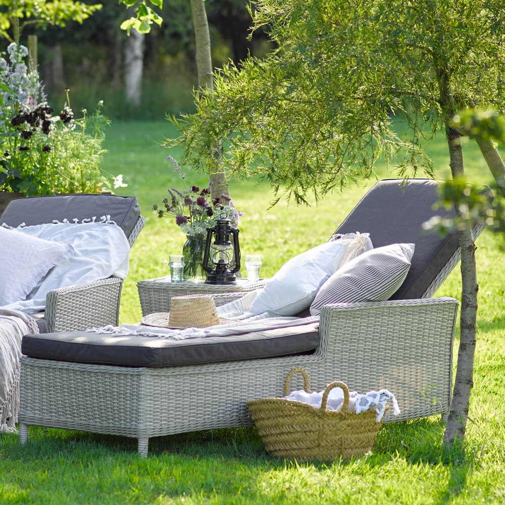 2 x Bramblecrest Monterey sun loungers on grass with cushions, throws and straw hats on them 