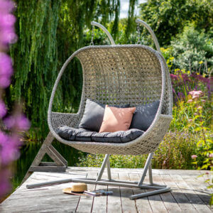 Hartman Heritage double hanging cocoon chair in ash and slate on deck with blurred purple flowers on left image edge
