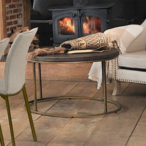 Wiltshire Round Coffee Table in Nutmeg. photoed in front of fireplace next to cream armchair