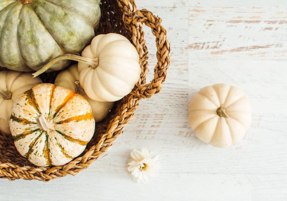 aerial close up of white pumpkins and squashes in wicker basket. 1 x white pumpkin on pale surface top