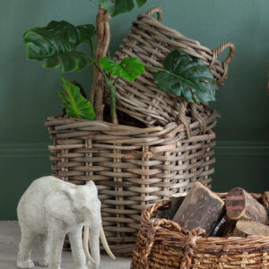 Wide weave baskets stacked with plant and elephant ornament with round basket with logs in foreground
