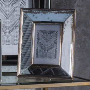 Large mirror photo frame with worn edges sat on glass shelf next to larger mirror photo frame