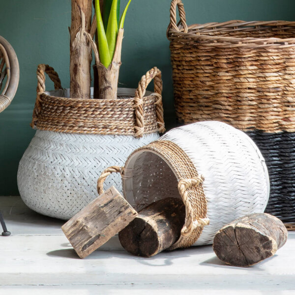 Two Rustica bamboo round baskets on white floor one with long plant sat inside upright basket and one basket spilling out split wood