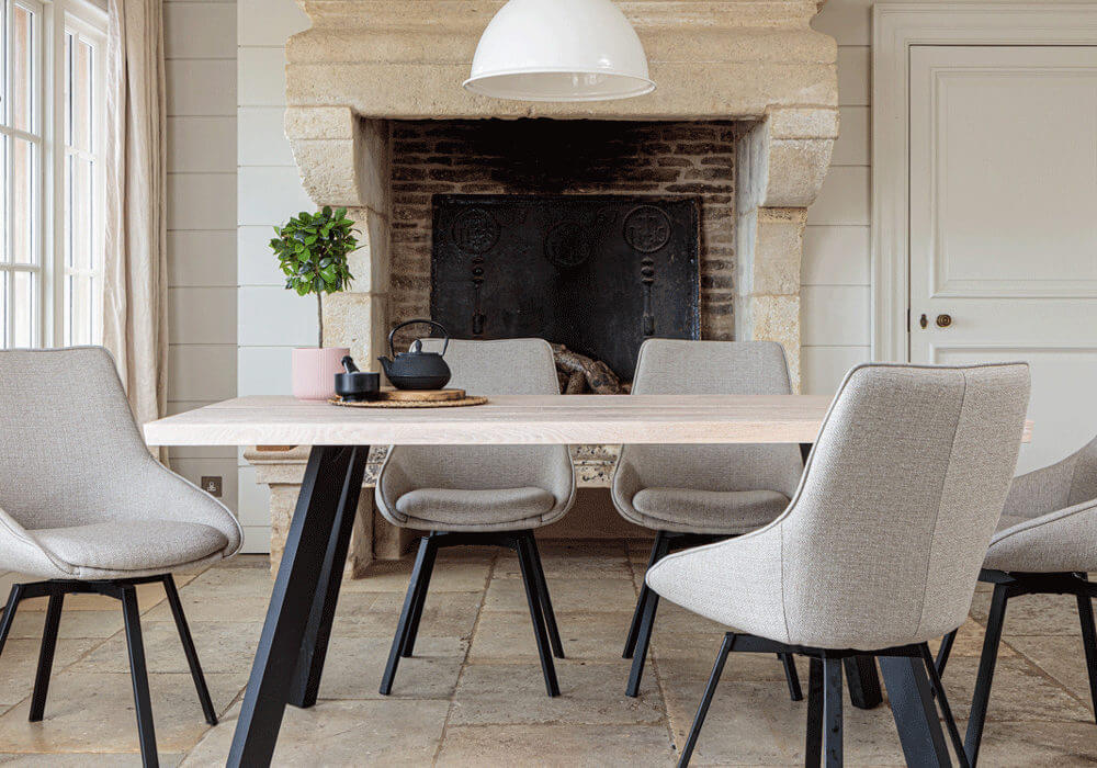 Valencia Light Oak Dining Set With 5 X Gaudi Light Grey Dining Chairs in front of large stone fireplace