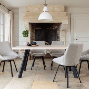 Valencia Light Oak Dining Set With 5 X Gaudi Light Grey Dining Chairs in front of large stone fireplace