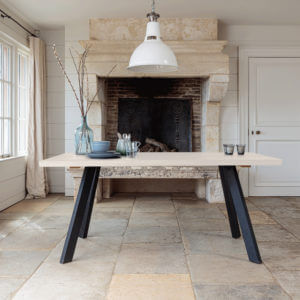 Valencia Light Oak Dining Table on stone floor in front of large fireplace
