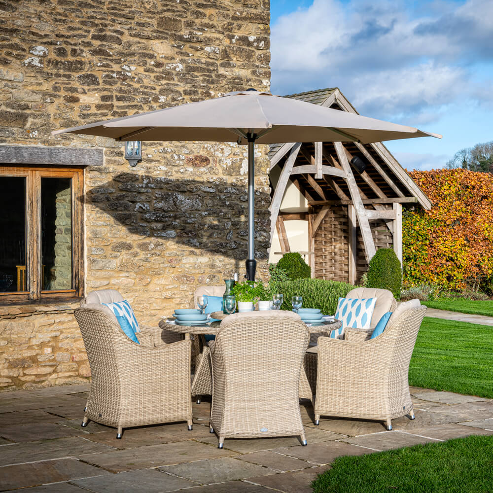 Bramblecrest Monterey 6 Seater Dining Table Set With Parasol On Paved Patio In front Of A Country House