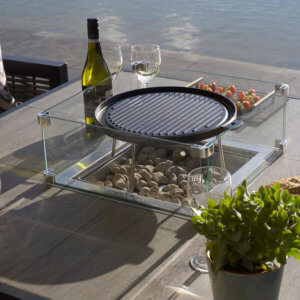 Bramblecrest Griddle with square bracket on firepit dining table with wine bottle and glasses next to it