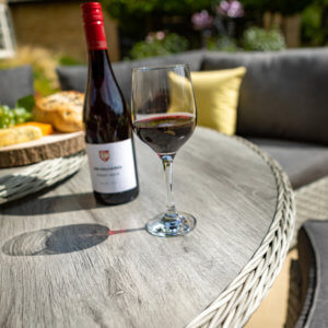 red_wine_glass_and_bottle_on_top_of_ceramic_table_in_sunshine
