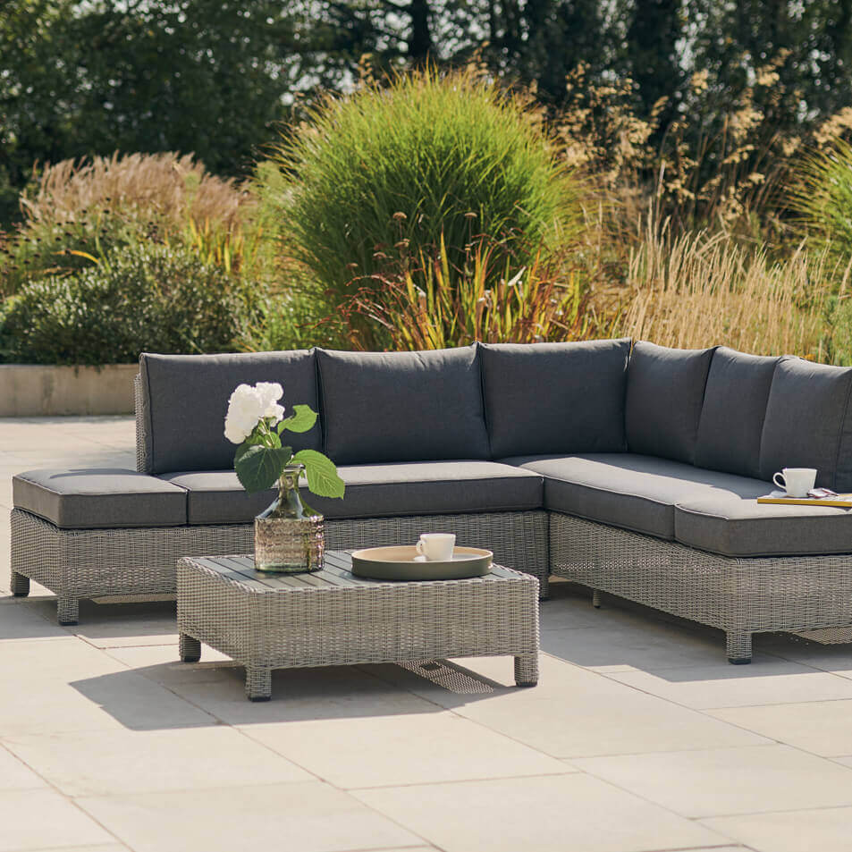 Kettler Palma low lounge corner sofa set placed on a garden patio with flowers and a tray on the coffee table