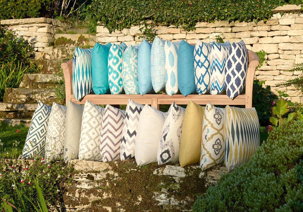 assortment of Bramblecrest scatter cushions placed on rows of outdoor shelves in a garden area