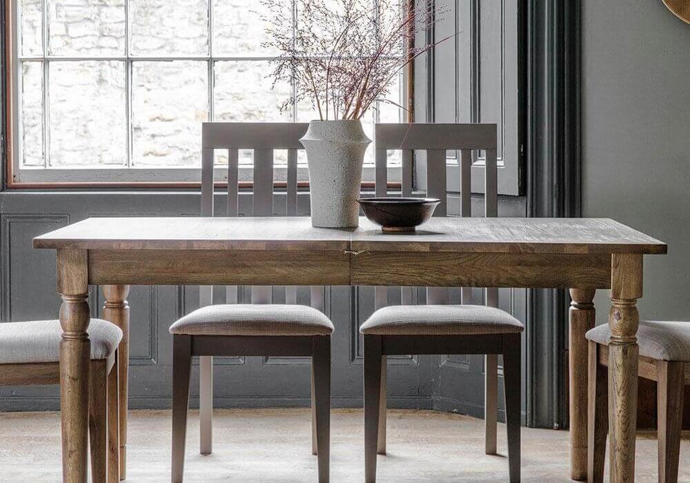 Rural extending oak dining table with a vase on top and two chairs