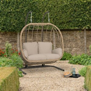 : Bramblecrest Chedworth Open Weave Double Cocoon with Season Proof Cushions - Sandstone - on outdoor gravel patio infront of stone wall
