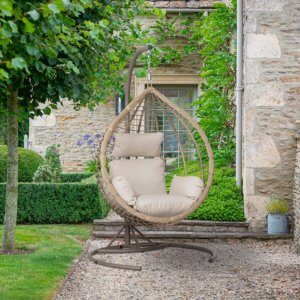 Bramblecrest Chedworth Tulip Open Weave Single Cocoon - Sandstone- on gravel patio next to stone house and tree