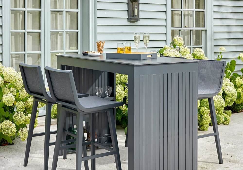 Bramblecrest La Rochelle 4 Seat Rectangle Garden Bar Table Set - Anthracite/Dark Grey on outsoor patio with yellow flowers next to house
