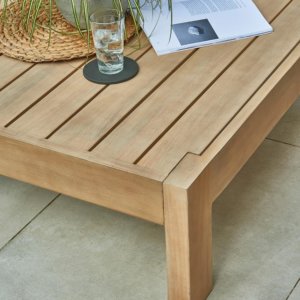 close up of wooden outdoor table with glass, magazine and plant on top