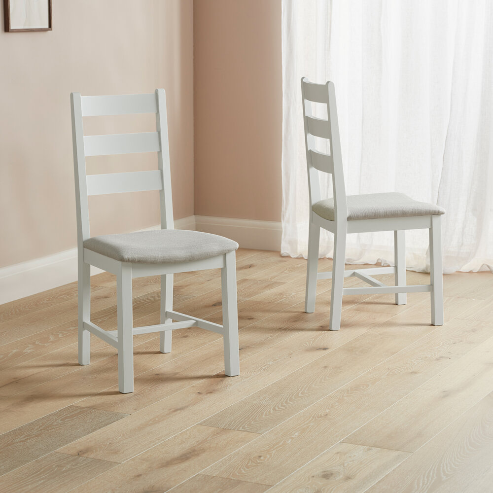 white dining chairs with strut back design and seat pads stood on wooden flooring in dusky shaded room