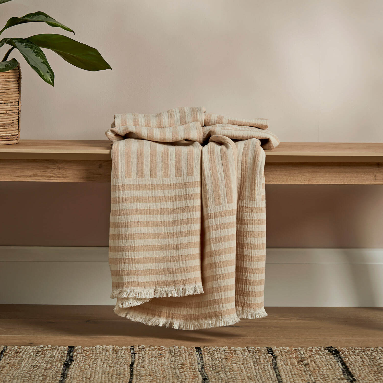 Cosdon throw in beige placed on a wooden bench with a plant placed to the side of it